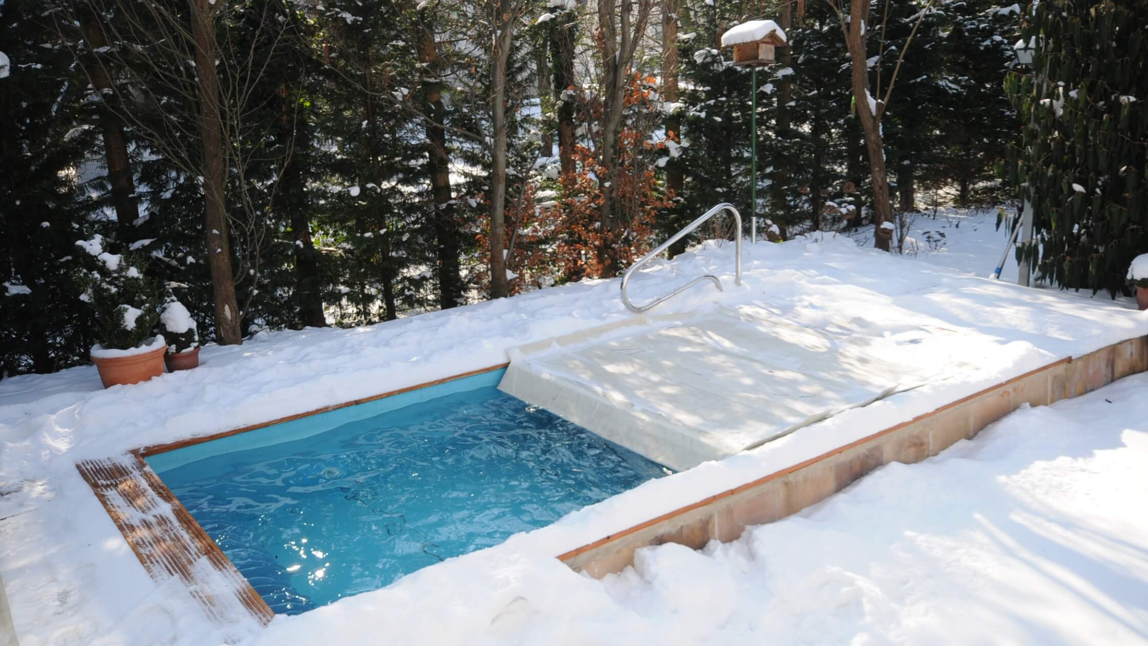 Ansicht einer LD POOL Gegenstromanlage im Winter im verschneiten Garten halbabgedeckt mit einer Poolabdeckung